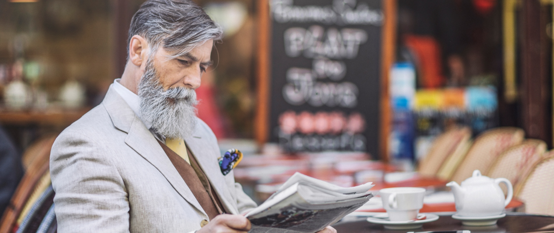 Gut gekleideter Herr in den besten Jahren sitzt in einem Straßencafé und liest Zeitun