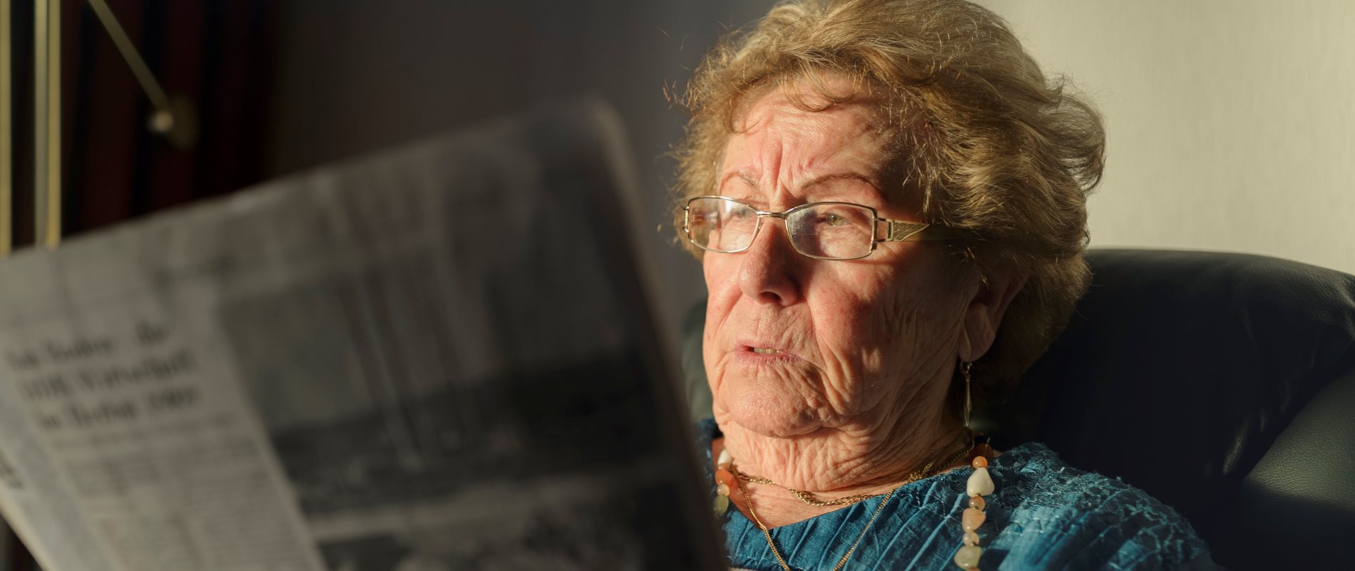 Ältere Dame liest gemütlich Zeitung in einem Armsessel